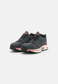 Zapatillas deportivas con una parte superior de malla gris oscuro y negro, acentuadas por detalles en rojo y blanco, que cuentan con una suela acolchada y una banda de rodadura texturizada.