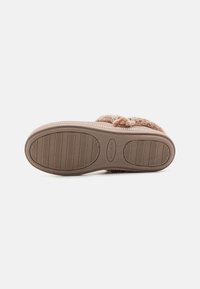 Semelle de pantoufle en fausse fourrure beige avec semelle en caoutchouc, dotée d'un fond texturé pour une meilleure adhérence et d'un nom de marque en relief. Forme arrondie pour plus de confort.