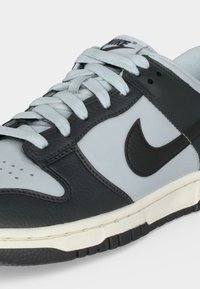 Χαμηλού τύπου αθλητικό παπούτσι Nike σε μαύρο και ανοιχτό γκρι δέρμα με λευκά κορδόνια και λευκή σόλα με μαύρες λεπτομέρειες πέλματος.