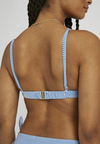 Haut de bikini rayé bleu et blanc avec des bretelles ajustables, un fermoir doré à l'arrière et une finition en tissu texturé.