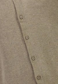 Beige stickad cardigan med ribbad textur och fem matchande knappar längs placket för stängning.