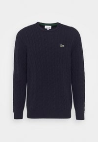 Suéter de punto de cable en color navy con mangas largas, puños y dobladillo acanalados, presenta un pequeño logo de cocodrilo verde en el lado izquierdo del pecho.