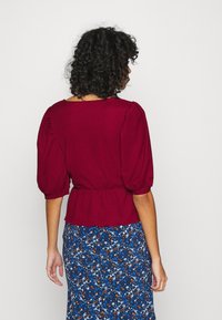 Bourgogne peplum top med puffede ærmer, struktureret stof og rund halsudskæring, sammen med en blå skørt med blomsterprint.