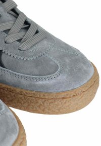 Sneaker in suede grigio con suola in gomma testurizzata, dotato di un design con lacci e accenti neri a contrasto sui lati.