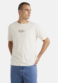 Cream-colored cotton t-shirt featuring a graphic logo in black and green on the chest. Short sleeves with a round neckline.