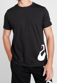 Black cotton t-shirt with short sleeves, featuring a large white abstract design on the lower side and a white logo on the sleeve.