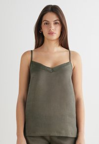 Oliwkowy leniany top na cienkich ramiączkach z dekoltem w kształcie litery V. Teksturowana powierzchnia z luźnym krojem, brak widocznych elementów metalowych lub wzorów.