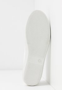 Semelle de sneaker blanche au revêtement texturé, présentant un logo circulaire avec le numéro 37. Arêtes lisses et design arrondi.