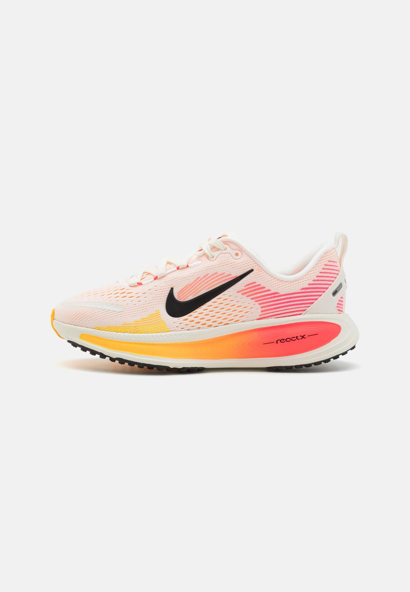 Zapatilla de running Nike en rosa claro con degradados en naranja y amarillo, parte superior de malla, logo Swoosh negro, suela acolchada y suela exterior de goma duradera.
