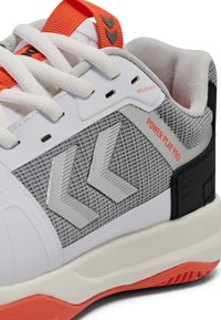Primer plano de una zapatilla blanca, gris y naranja con cordones blancos, panel lateral texturizado y el texto "POWER PLAY PRO" en una suela deportiva.