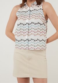 Biała bezrękawnik z wyszywanymi kwiatowymi wzorami w kolorach czerwonym, niebieskim, zielonym i czarnym. Zestawiony z beżową spódnicą dżinsową z przednimi kieszeniami.