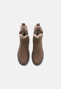 Bruine leren enkelboots met beige bontvoering, zwarte zolen en trekstraps, van bovenaf gezien op witte achtergrond.