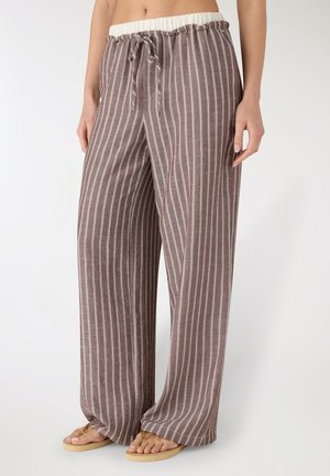 Pantaloni a gamba larga a righe verticali marroni e bianche con vita a coulisse, indossati con infradito beige da una persona in piedi.