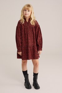 Sarkans kleita ar melnu leopardu rakstu, garām piedurknēm un savākta yoke. Valkāta ar melniem potīšu zābakiem un melniem zeķēm. Vienkāršs, brīvs piegriezums.