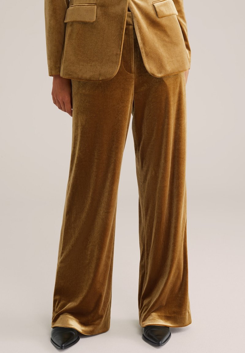 Pantalon large en velours marron associé à un blazer assorti et des chaussures noires à bout pointu sur une personne debout.