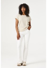 Camiseta a rayas beige y blanca con mangas enrolladas, combinada con pantalones blancos. El conjunto se completa con zapatillas de deporte beige claro.