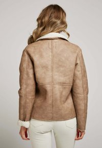 Veste en cuir synthétique marron avec col en shearling, présentant un design ajusté, des coutures visibles et une finition texturée. Vue de dos montrée.