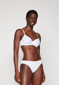 Sutien alb, fără cusături, cu bretele ajustabile și o textură netedă; asociat cu chiloți albi, cu talie joasă, într-un design minimalist.