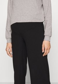 Top gris de manga larga combinado con pantalones anchos negros. El top tiene una textura suave, mientras que los pantalones presentan una textura acanalada y una cintura elástica.