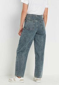 Havenblauwe hoge taille wijde jeans met een vervaagde afwerking, contrasterende stiksels en vier zakken. Gestyld met een wit T-shirt en sneakers.