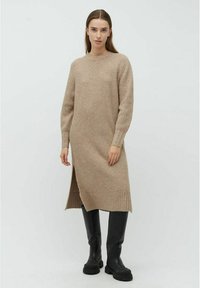 Beige ribbet strikkjole med lange ærmer og sideskår, parret med knæhøje sorte støvler. Glat tekstur og tætsiddende silhuet.