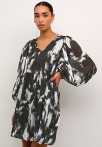Robe plissée noir et blanc avec un décolleté en V, des manches longues bouffantes et un motif abstrait, présentant une coupe décontractée et un léger cintrage à la taille.