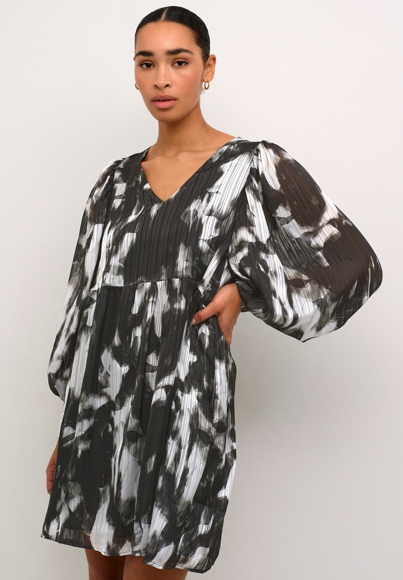 Robe plissée noir et blanc avec un décolleté en V, des manches longues bouffantes et un motif abstrait, présentant une coupe décontractée et un léger cintrage à la taille.