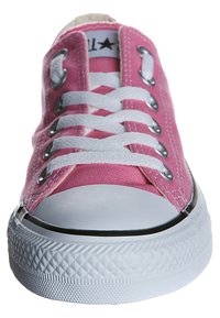 Zapatilla de lona rosa con cordones blancos, puntera de goma blanca y suela texturizada, vista desde el frente.