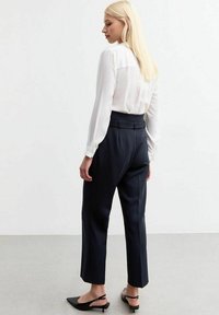 Witte blouse met lange mouwen, gecombineerd met donkerblauwe op maat gemaakte broek met een hoge taille en rechte benen. Zwarte ballerina's maken de look compleet.