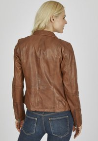 Braune Lederjacke mit tailliertem Design, sichtbaren Nähten und Reißverschlüssen an den Ärmeln. Strukturierte Oberfläche, Rundhalsausschnitt und mittellange Ausführung.