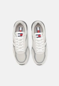 Baskets en mesh blanches avec des accents gris, bout rond et lacets plats. Présente une étiquette logo avec des couleurs rouge, blanc et bleu sur la languette.