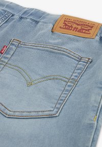 Ljusblå jeans i denim med en distinkt bakficka, gul söm och en brun läderetikett med Levi's-logotypen.