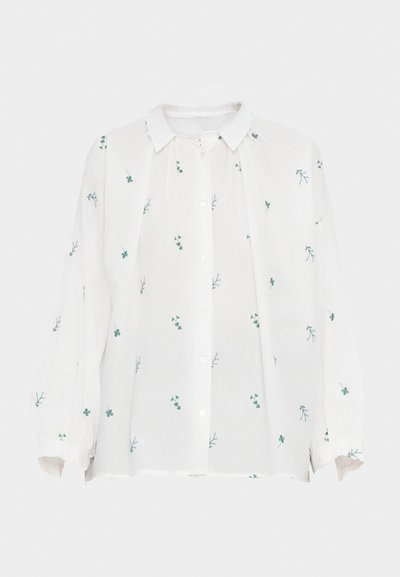 Chemise en lin blanc avec un devant à boutons. Présente des broderies florales vertes et bleues, des manches longues et un col pointu. Coupe décontractée.
