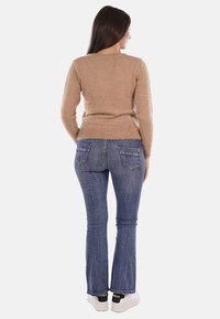 Maglione beige morbido con collo rotondo, aderente in vita. Abbinato a jeans a zampa d'elefante di colore blu scuro, con tasche posteriori, indossato con sneakers bianche.