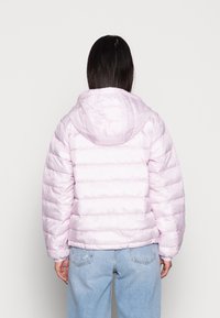Giacca piumino rosa chiaro con cappuccio, caratterizzata da cuciture orizzontali e polsini elastici, abbinata a jeans a vita alta di un blu chiaro.