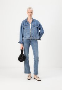 Denim-takki rentoa istuvuutta, vaaleansininen väri ja etunapit. Yhdistetty tiukkoihin sinisiin farkkuihin ja mustaan laukkuun, jossa on kukkakoristeet.