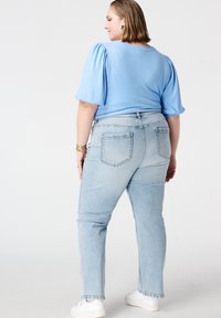 Haut bleu clair à manches bouffantes associé à un jean bleu délavé à jambes droites. Baskets blanches, bracelet discret et finition en tissu texturé sur les deux articles.