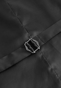 Eine Nahaufnahme einer schwarzen Stoffoberfläche zeigt eine silberne Metallschnalle und einen Riemen, die schlanke und minimalistische Designelemente präsentieren.