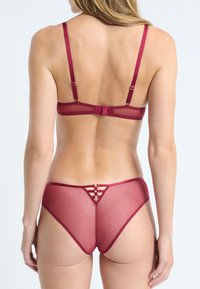 Set di lingerie bordeaux con reggiseno trasparente sul retro e spalline regolabili, abbinato a uno slip trasparente con dettagli a strisce orizzontali.
