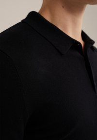 Svart pikétröja i stickad tyg. Har en klassisk krage och en slät textur, med en subtil glans och en skräddarsydd passform.