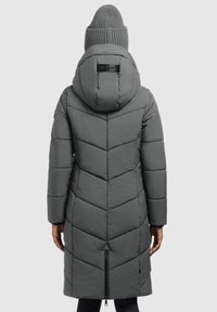 Cappotto lungo grigio in piuma con un motivo a zigzag, cappuccio e dettaglio con zip in fondo. Abbinato a un berretto di lana.