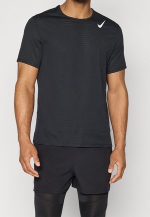 Homme portant un t-shirt Nike noir perforé à manches courtes, un short noir et des leggings noirs sur un fond clair uni.