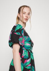 Vestido preto com flores, com mangas bufantes; apresenta grandes folhas verdes e flores rosas sobre um tecido texturizado; cintura justa e design até ao joelho.
