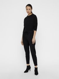 Jersey negro de punto con mangas largas; pantalones grises texturizados con cintura ajustable; botines negros con punta afilada.
