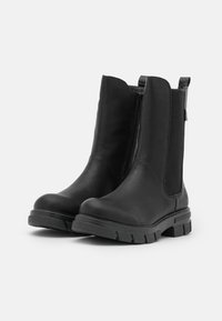 Bottes noires à la cheville en cuir lisse avec des panneaux élastiques sur les côtés, bout rond et semelle en caoutchouc texturée pour une meilleure adhérence. Détail de fermeture éclair sur un côté.