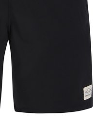 Zwarte knielange shorts met een klein wit rechthoekig logoplaatje met de tekst "Protest" nabij de onderzoom op het rechterbeen.