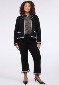 Černá zkrácená bunda se stříbrnými třásněmi, doplněná o vzorovanou černobílou blůzu a ladící černé zkrácené kalhoty. Černé boty.