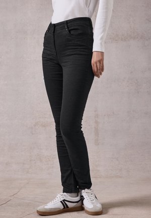 Jeans skinny neri in denim con una texture liscia, vita alta, leggera scoloritura e classico design a cinque tasche, abbinati a sneakers bianche.