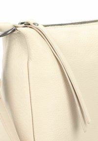 Borsa in pelle crema con angolo che mostra la texture a granulosa, attacco con anello metallico e zip con doppie linguette in pelle.