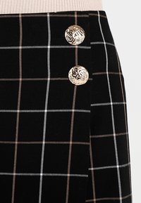 Sort ternet nederdel med hvid og beige rutenet mønster, der har to dekorative metalknapper foran. Damask stof, glat tekstur.